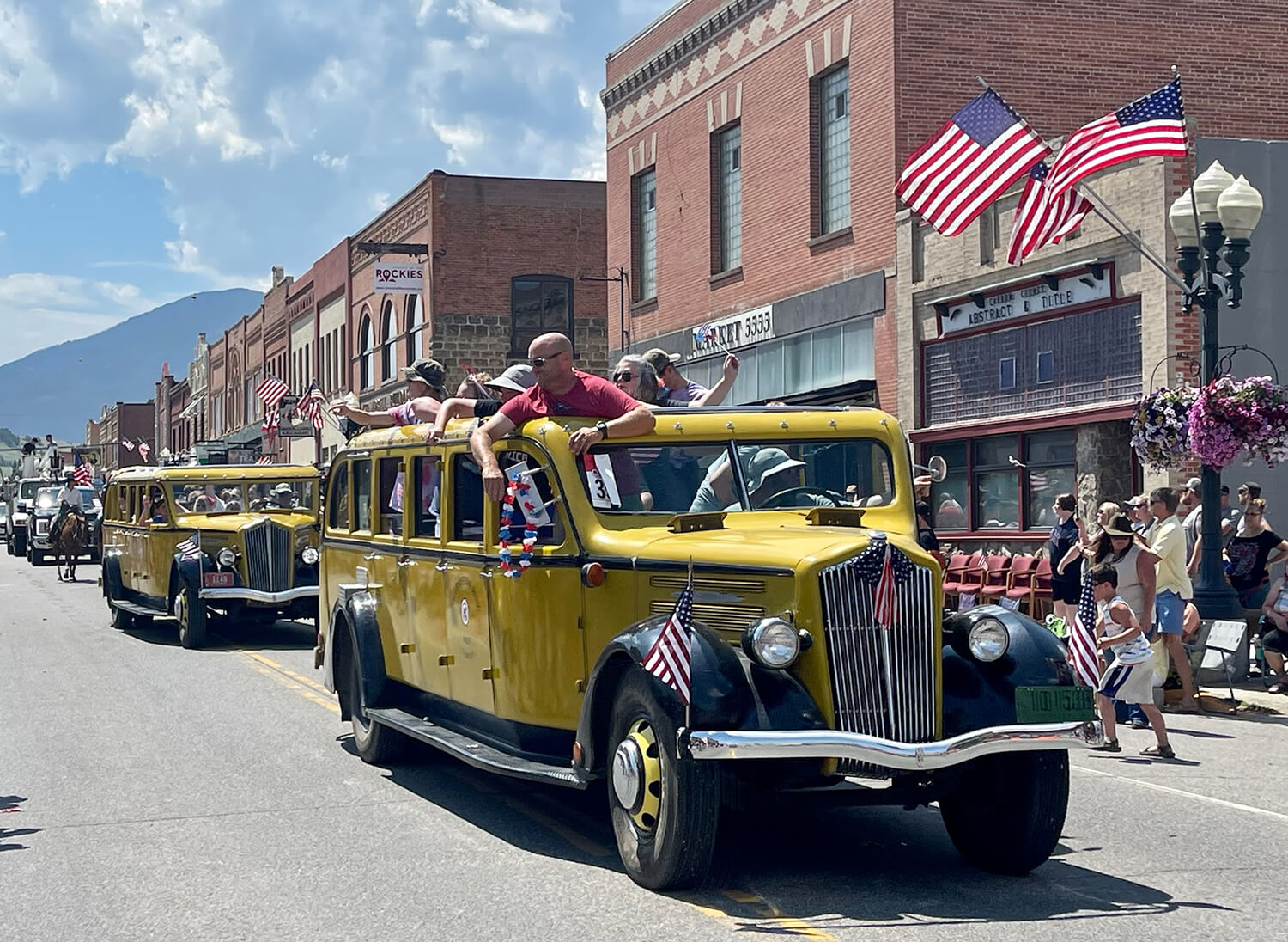 Yellow vintage buses in a patriotic parade.