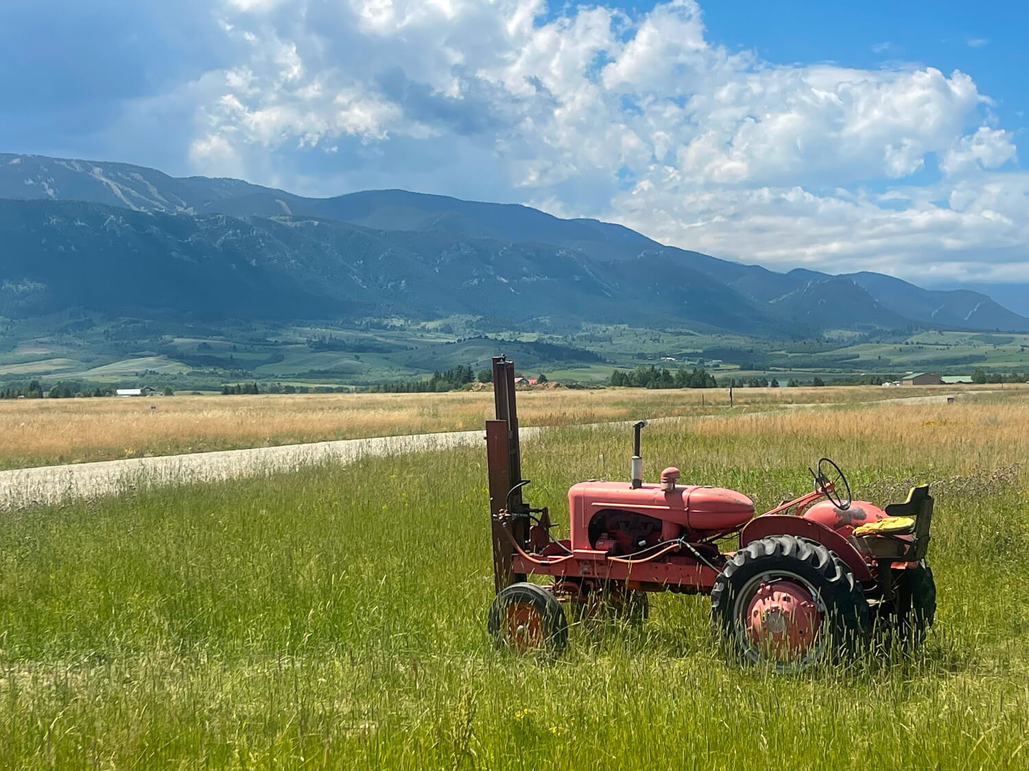 Red tractor in grassy field, mountains behind.